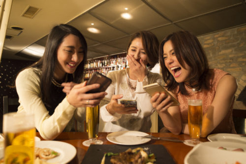 Three women are laughing while looking at the smartphone